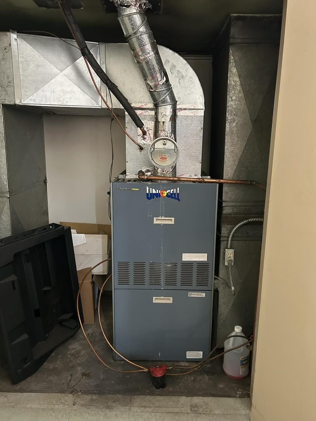 Basement furnace with silver ductwork and gray HVAC unit against cinder block walls.