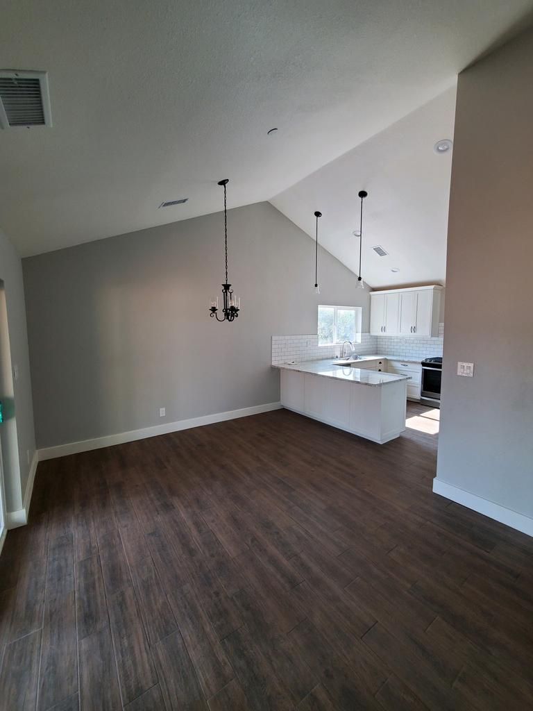 An empty room with a vaulted ceiling and a kitchen in the background.