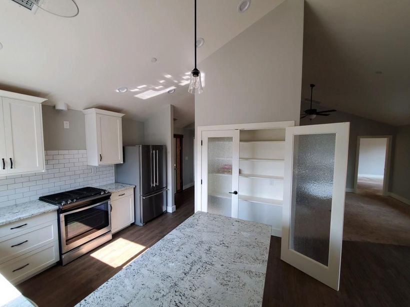 A kitchen with white cabinets , a stove , a refrigerator , and a ceiling fan.