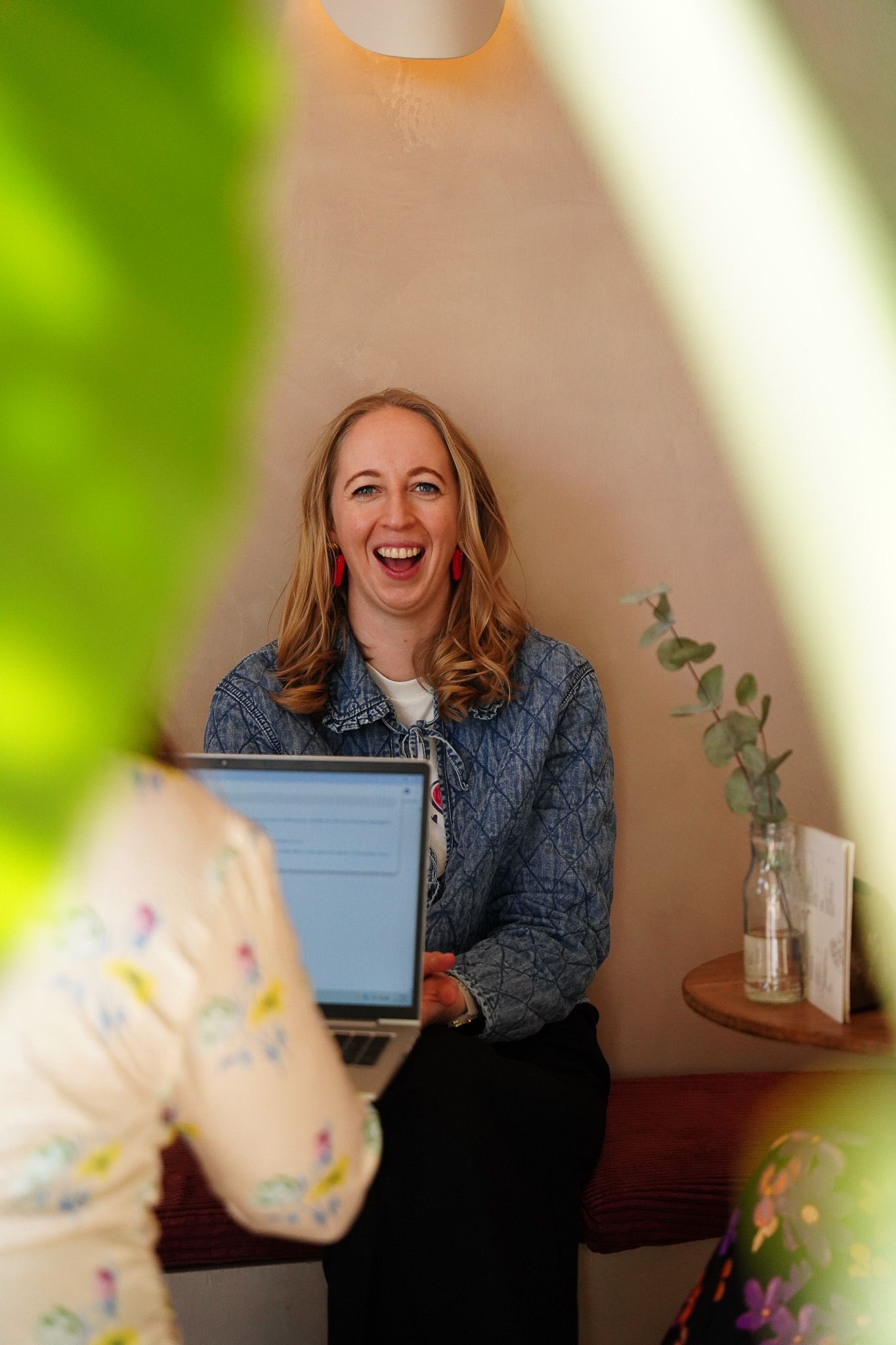 A woman is sitting at a table with a laptop and laughing.