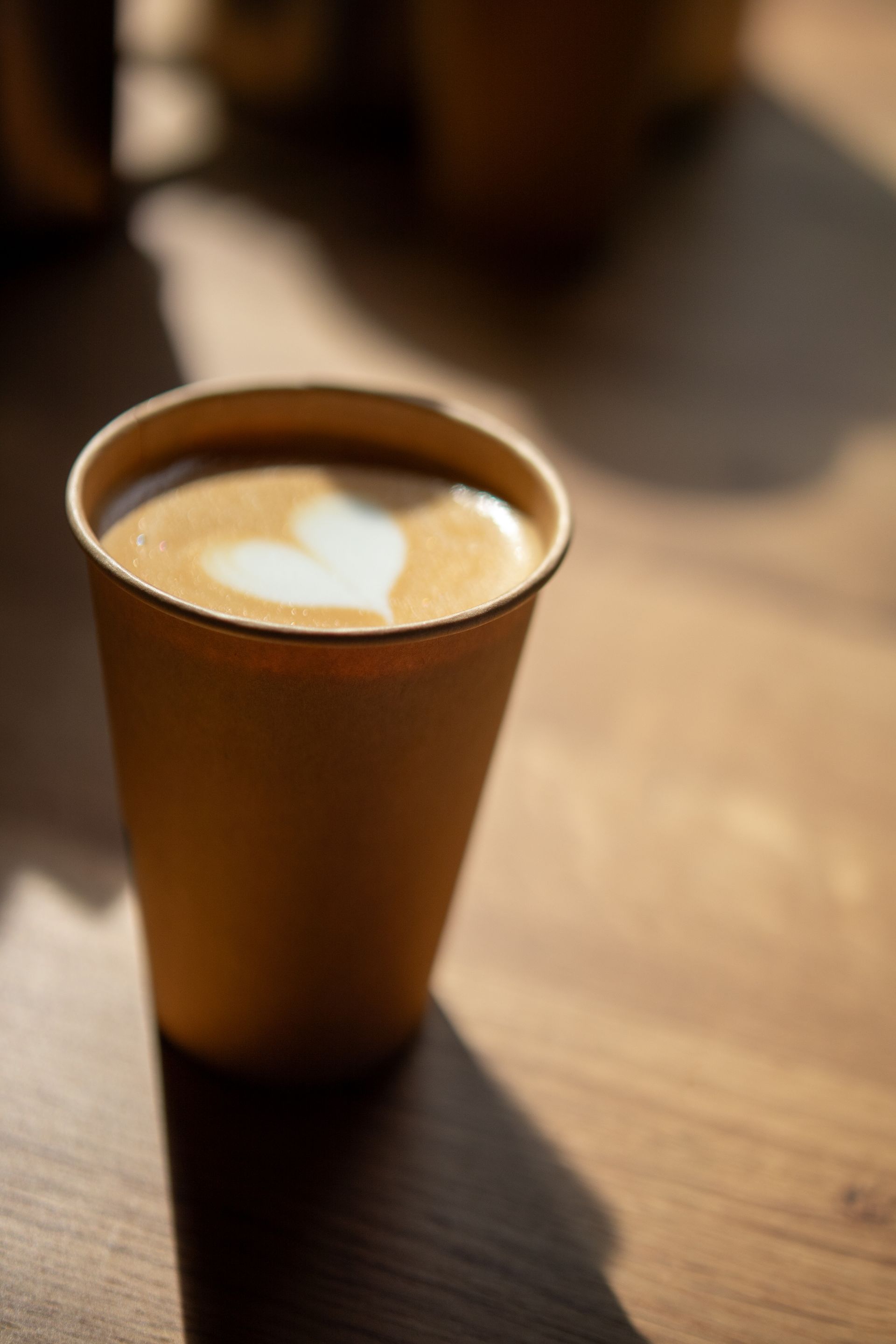 A cup of coffee with a heart in the milk is on a wooden table.