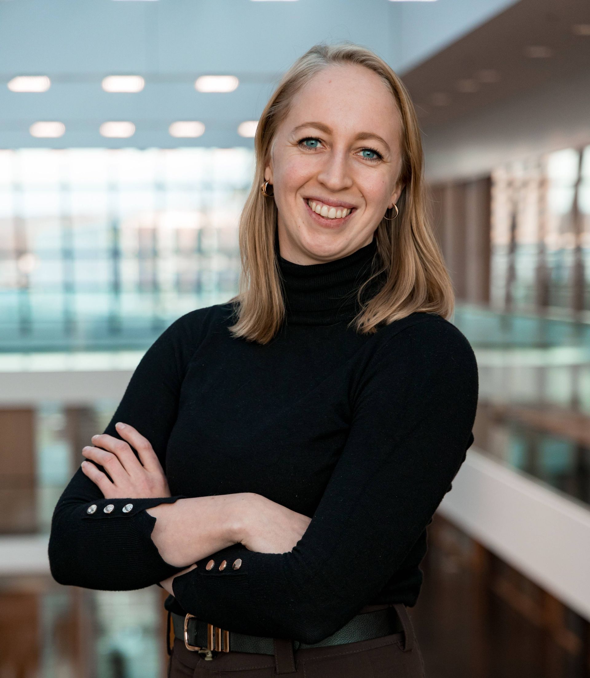 A woman in a black turtleneck is smiling with her arms crossed.