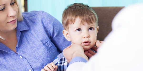 A child is examined by a medical professional while seated with a woman.