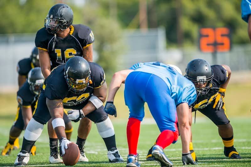 Football players in black and gold uniforms line up against a player in blue.
