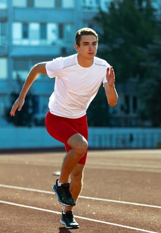 Man in white shirt and red shorts running on a track.