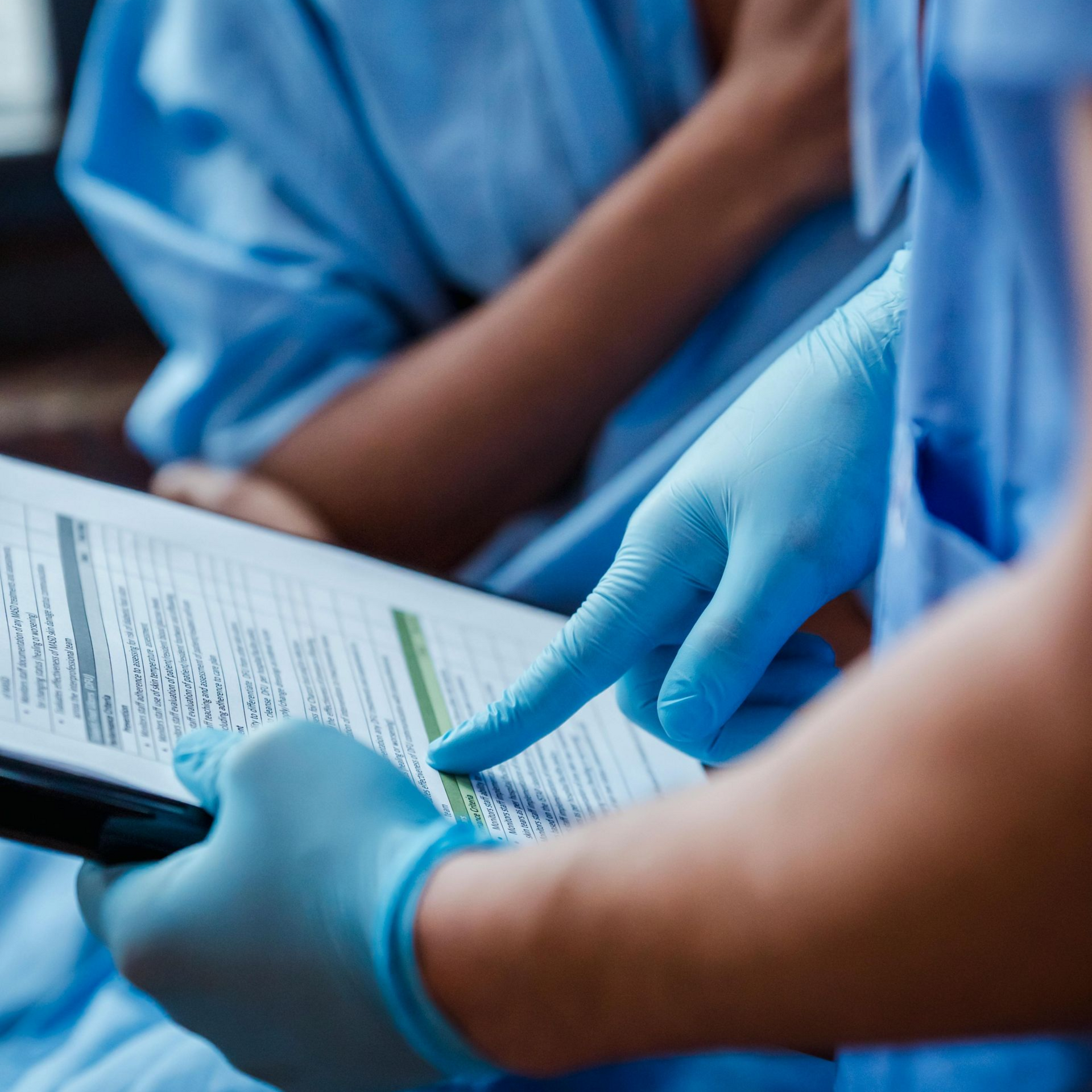 Person in blue gloves pointing at paperwork held by another person in a hospital setting.