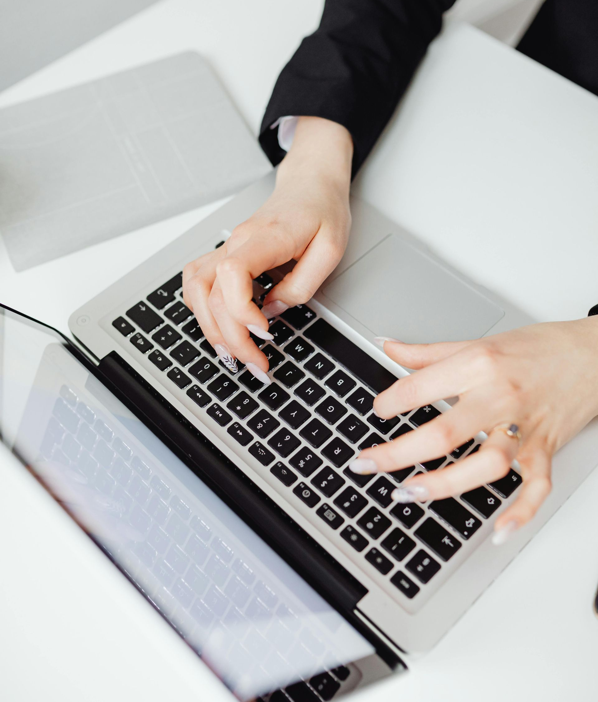Person typing on a laptop with two other laptops on a white desk.