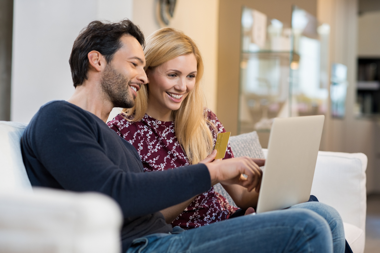 A man and a woman sitting on a couch looking at a laptop, with solar tint in San Antonio applied to the nearby windows.