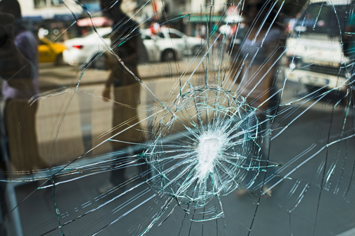 A close-up of a broken glass window with a hole, illustrating the need for security film in San Antonio.