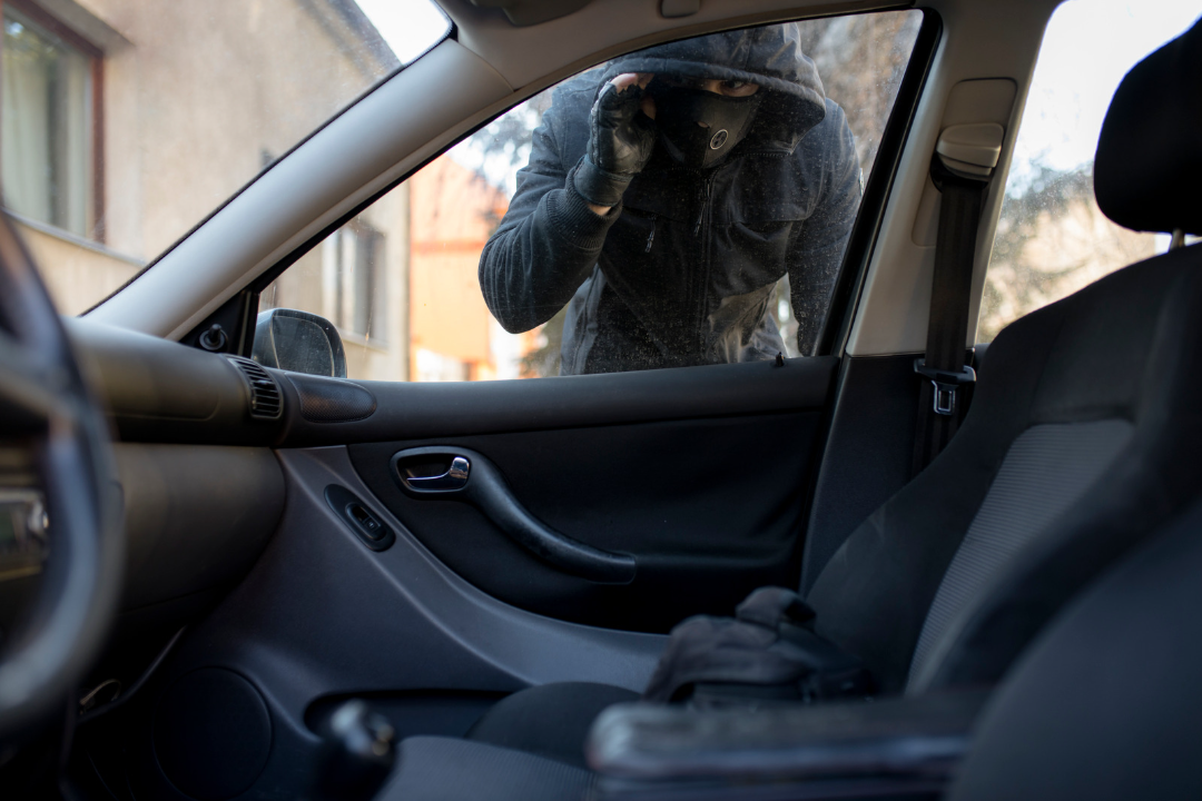 A man in a hooded jacket is breaking into a car.