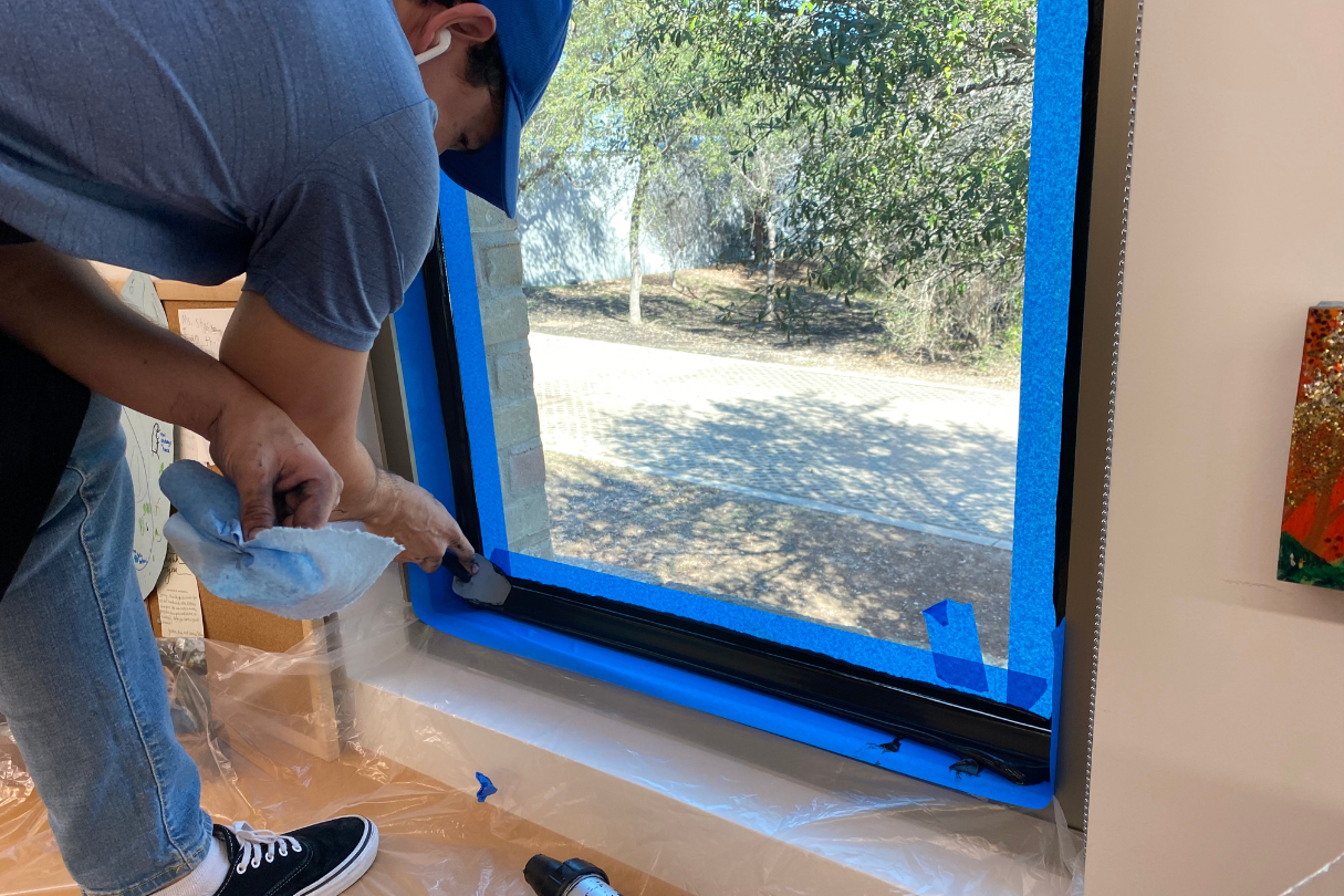 A man is painting a window with blue tape.