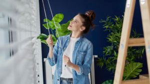 A woman is standing next to a ladder in a room holding a plant.