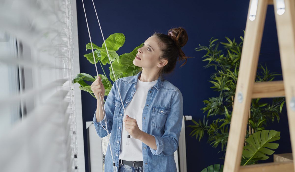 A woman is standing next to a ladder holding a plant.