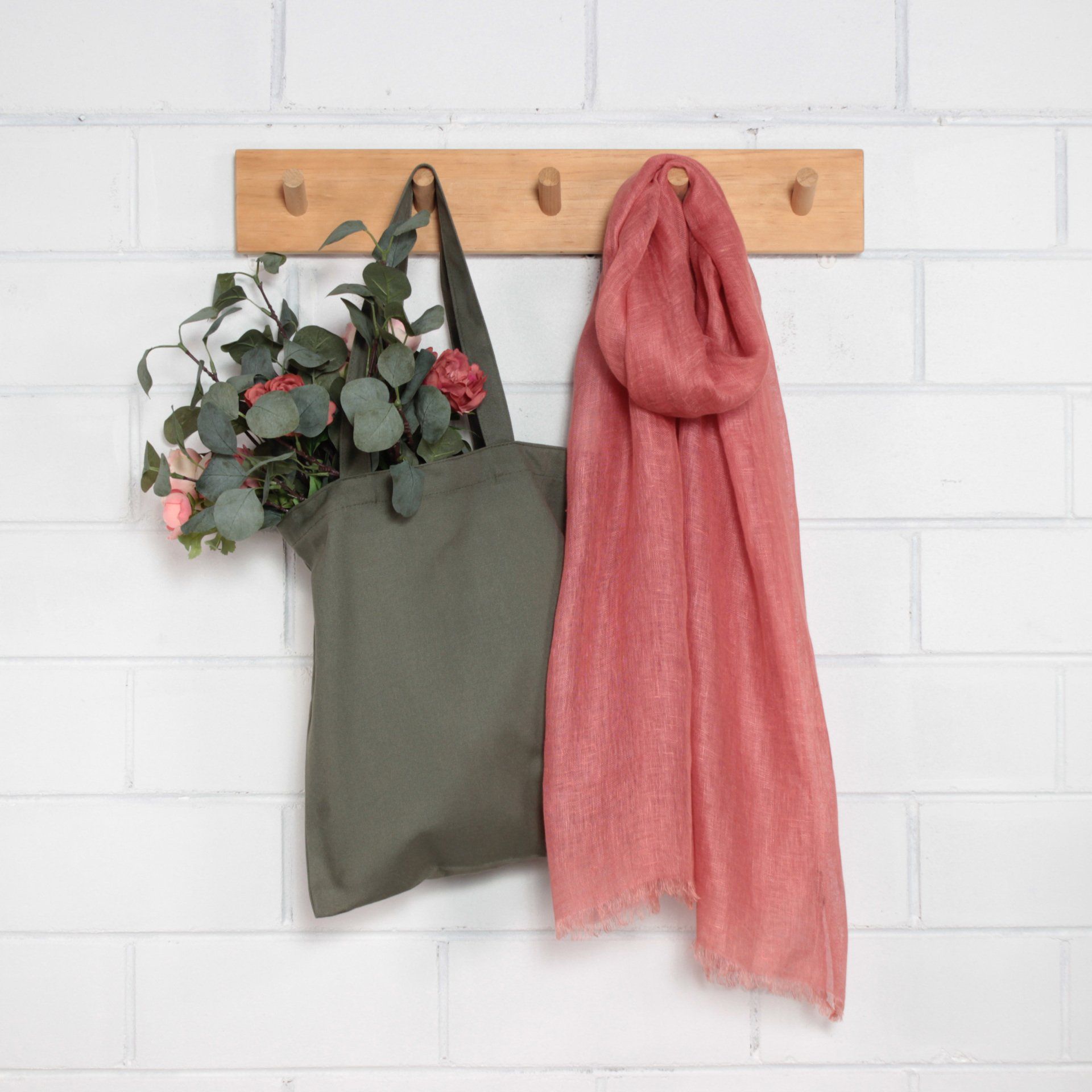 A green tote bag and a pink scarf are hanging on a wooden rack.