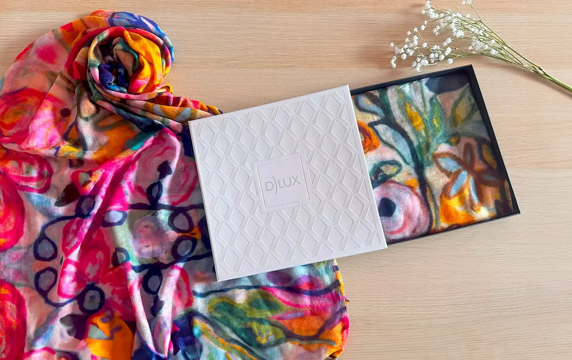A colorful GIFT BOXED DLUX scarf is sitting on top of a wooden table next to a card.