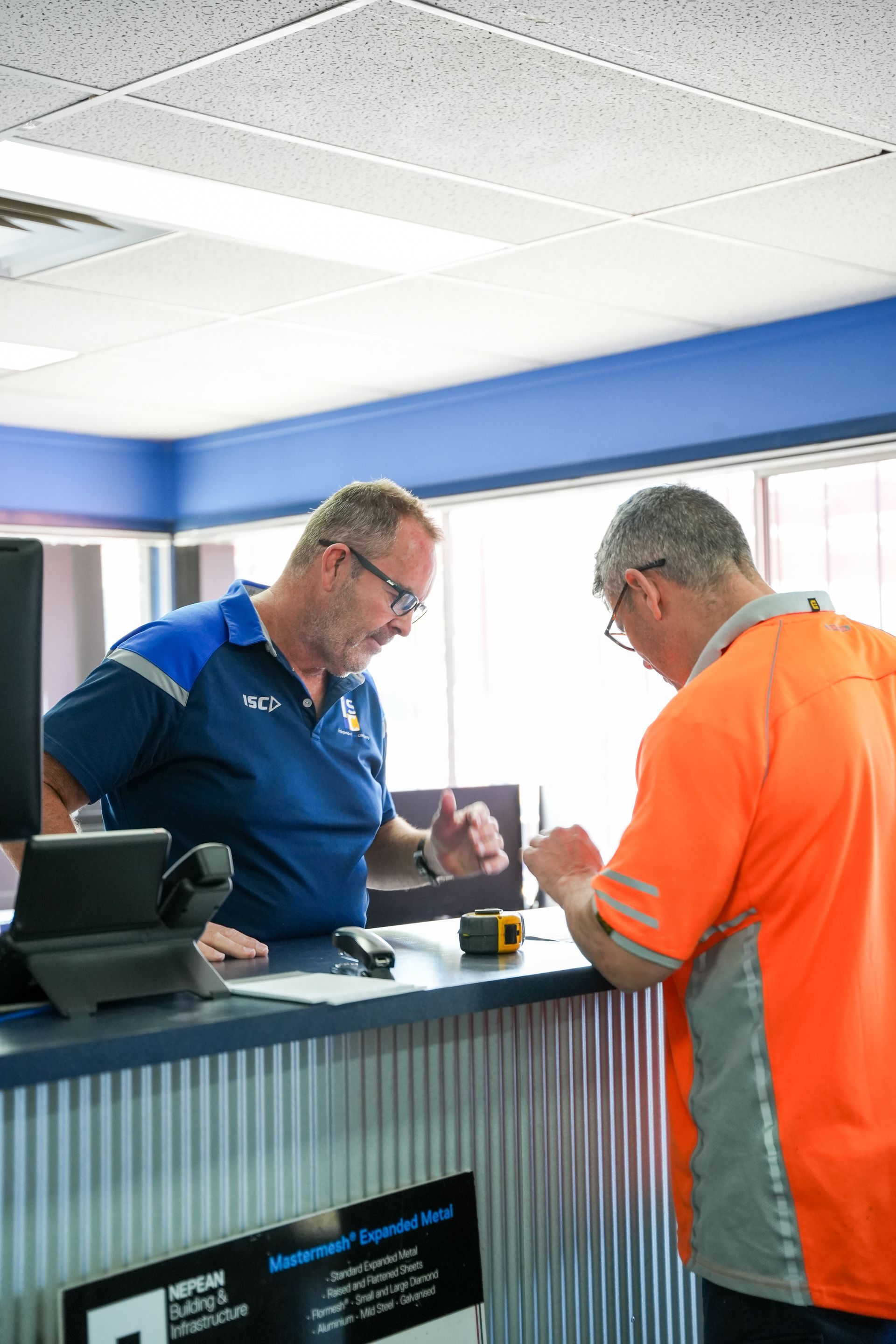 A worker wears heavy-duty gloves while operating a metal press brake to bend a piece of sheet metal.