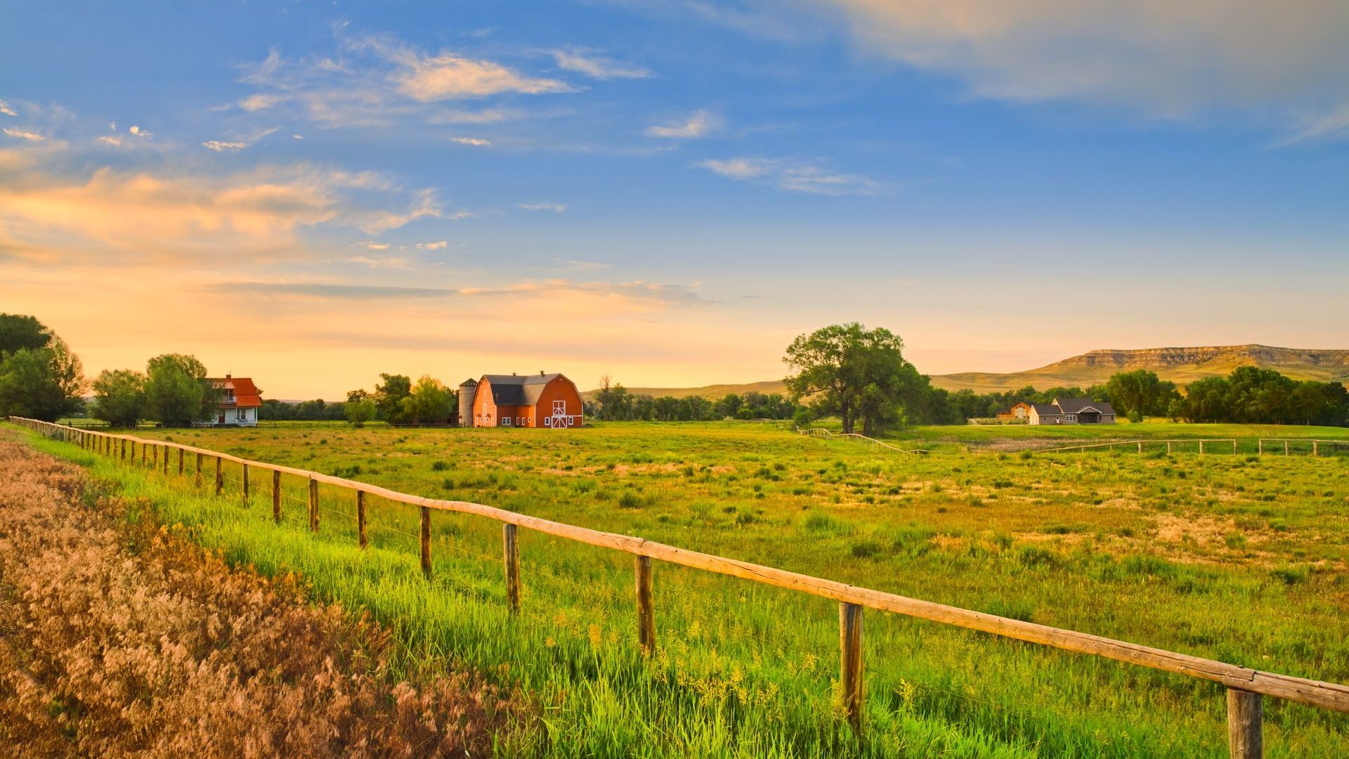 A wooden fence surrounds a grassy field with a barn in the background.