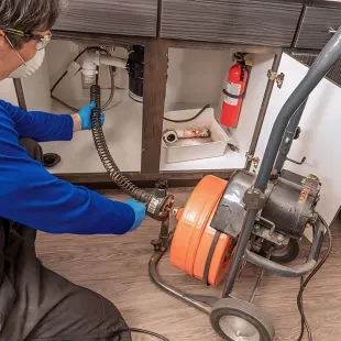 Doctor Cool - A man is using a machine to clean a drain under a sink.