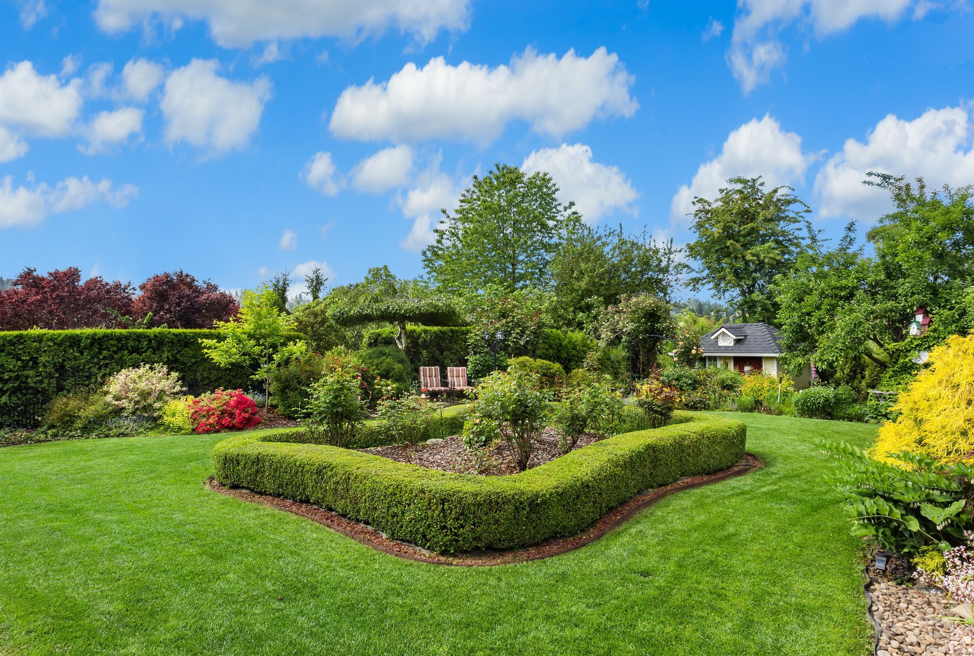 Lush garden with manicured hedges, colorful flowers, and a bright blue sky with clouds