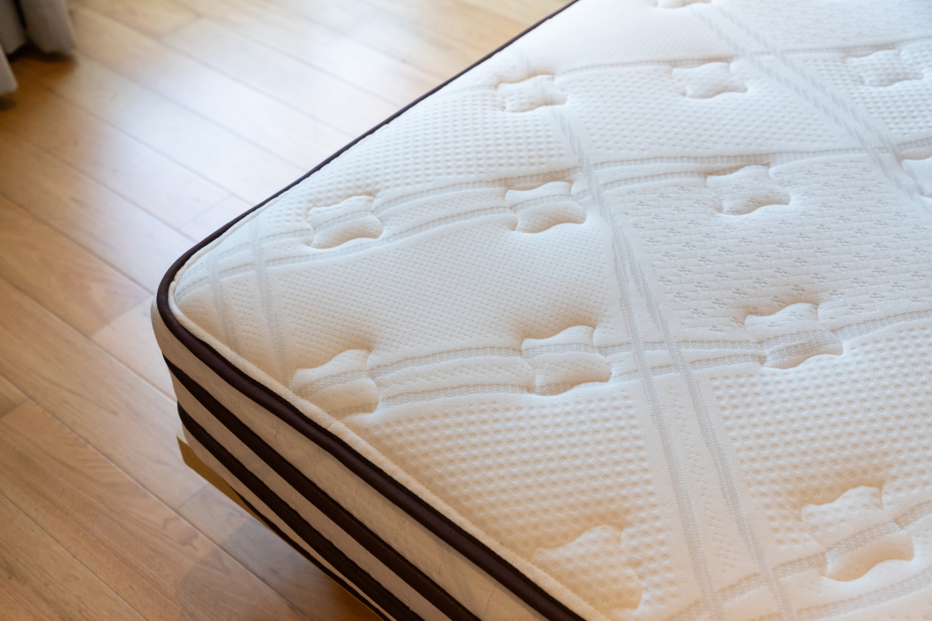 A white mattress is laying on a wooden floor.