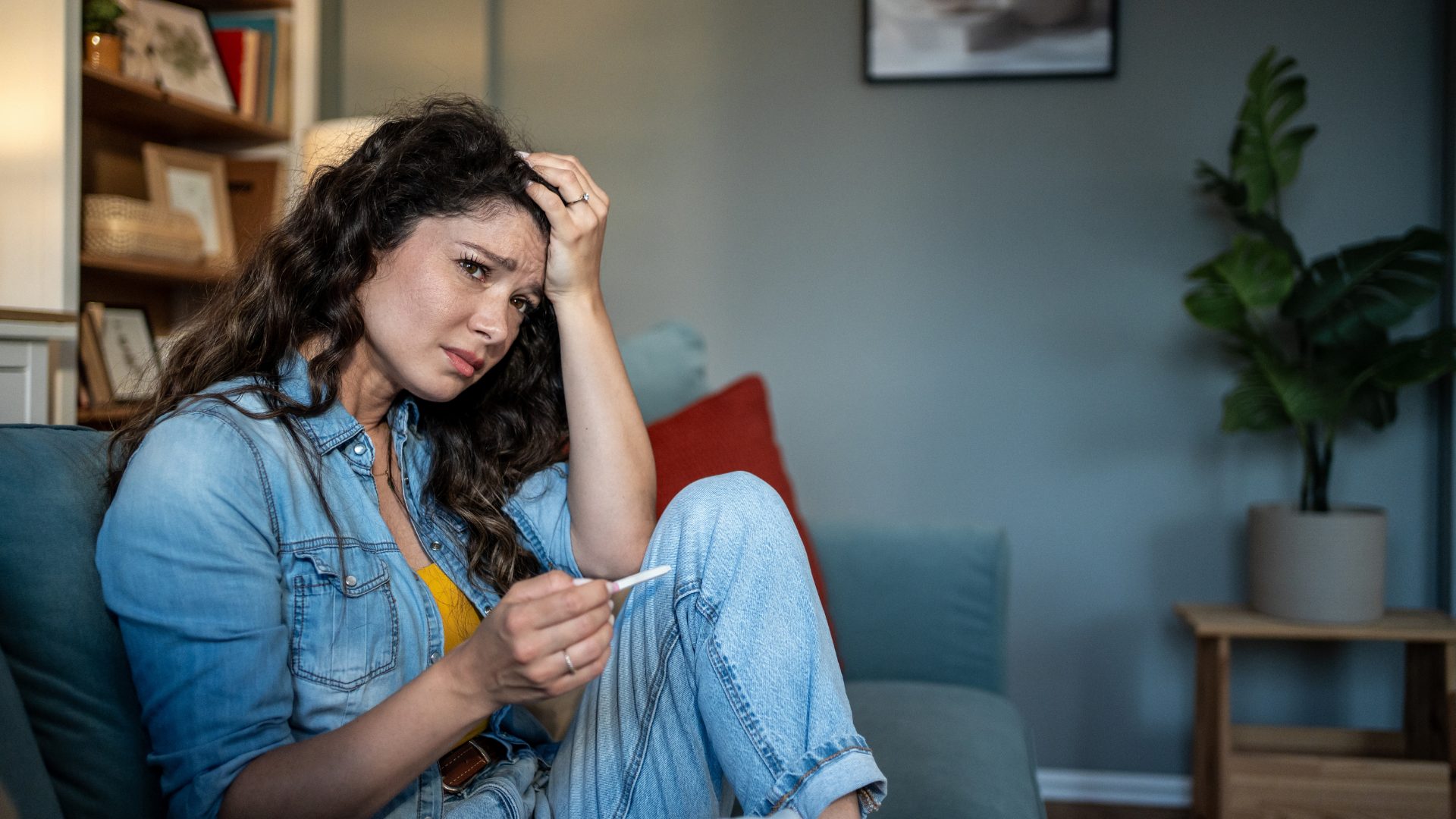 Woman on sofa, distressed, holding a pregnancy test.