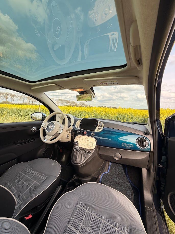 Klassiek auto-interieur met wit stuurwiel en beige dashboard, met uitzicht op gele velden door de ramen.
