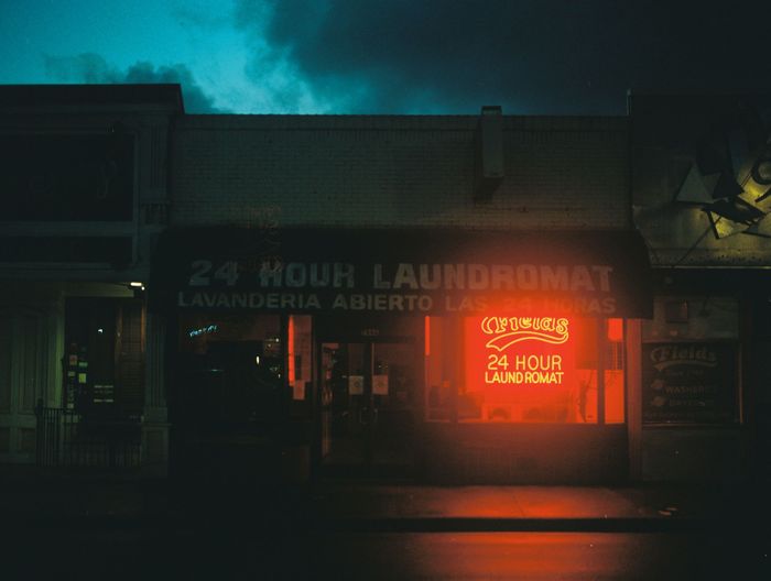 Exterior of 24 hour laundromat with glowing neon sign at night