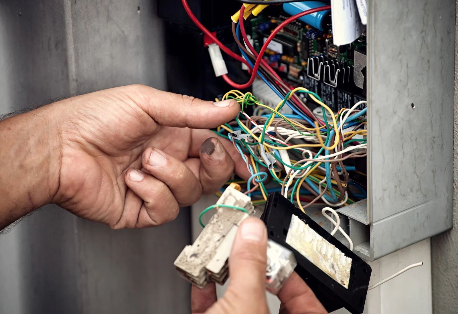 Hands working on an open electrical box, with tangled wires and components visible.