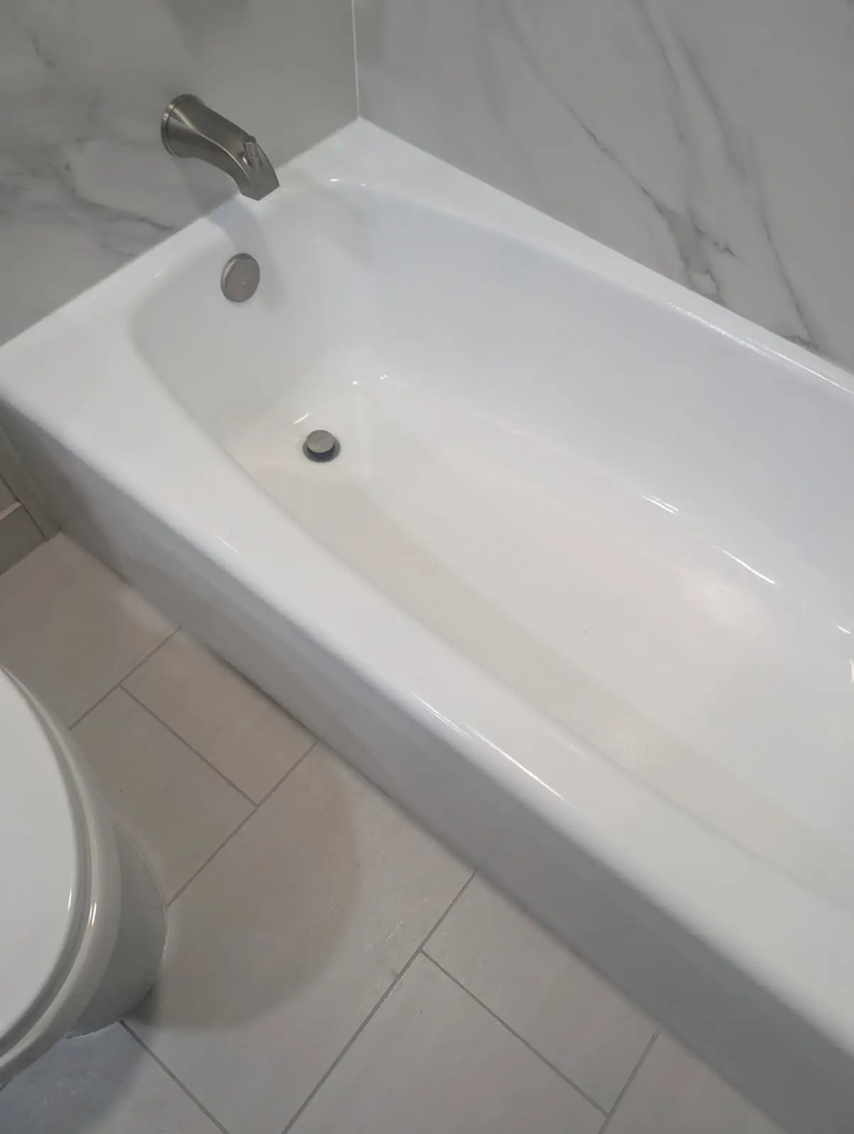 White bathtub with chrome faucet in a tiled bathroom, next to a partially visible toilet.
