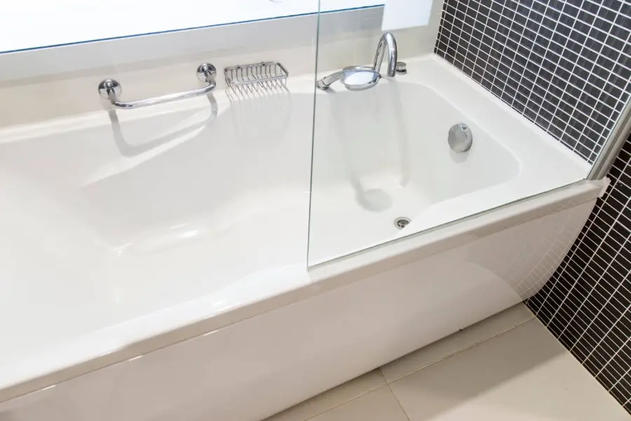 Bathtub with glass shower screen, chrome faucet, and mosaic tile wall in a bathroom