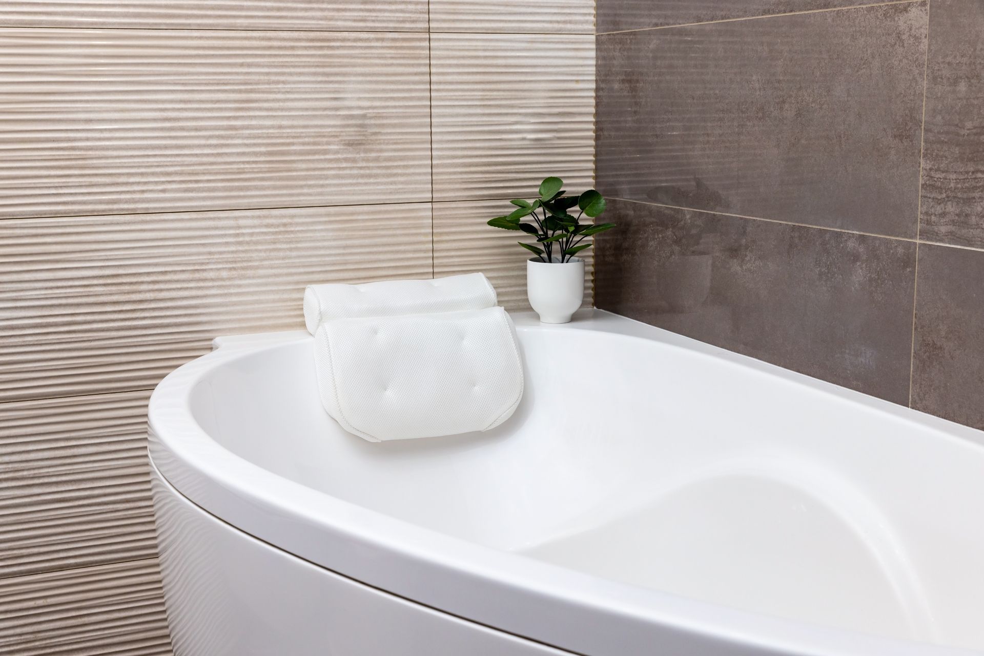 Modern bathtub with rolled white towel and small potted plant against tiled bathroom wall