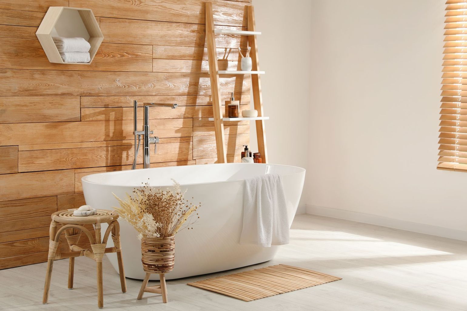 Modern rustic bathroom with freestanding tub, wooden wall, stool, and woven mat in warm sunlight