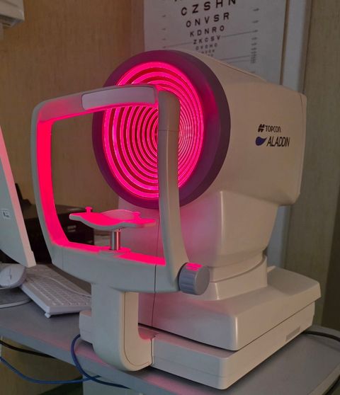 Ottico che utilizza un apparecchio per l'esame della vista su un paziente, in un ambiente medico bianco.