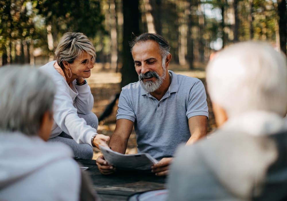 Group of seniors outdoors, reading a paper together in a forest setting, smiling.