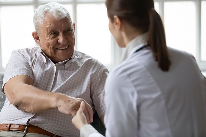 Elderly man shaking hands with a doctor, both smiling. They're indoors, suggesting a medical setting.