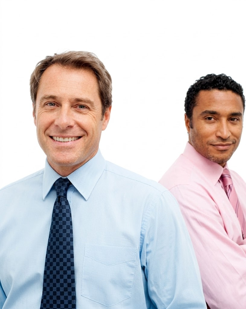 Two men standing back to back, smiling in light blue and pink dress shirts with ties.