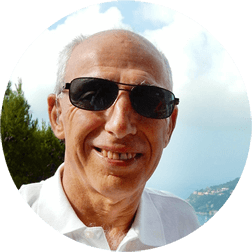 Smiling man in sunglasses and white shirt outdoors with sky and sea behind him