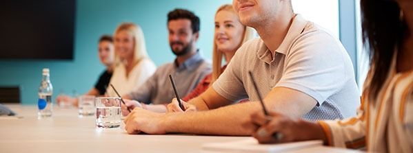 People seated at a conference table in a meeting room, listening attentively.