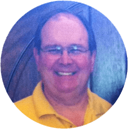 Smiling man in glasses wearing a yellow polo shirt against a blue-gray background