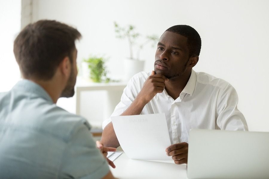 Two people in a bright office meeting, one holding papers and listening thoughtfully across a desk.