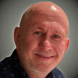 Bald man with a slight smile, wearing a dark blue shirt; gray background.