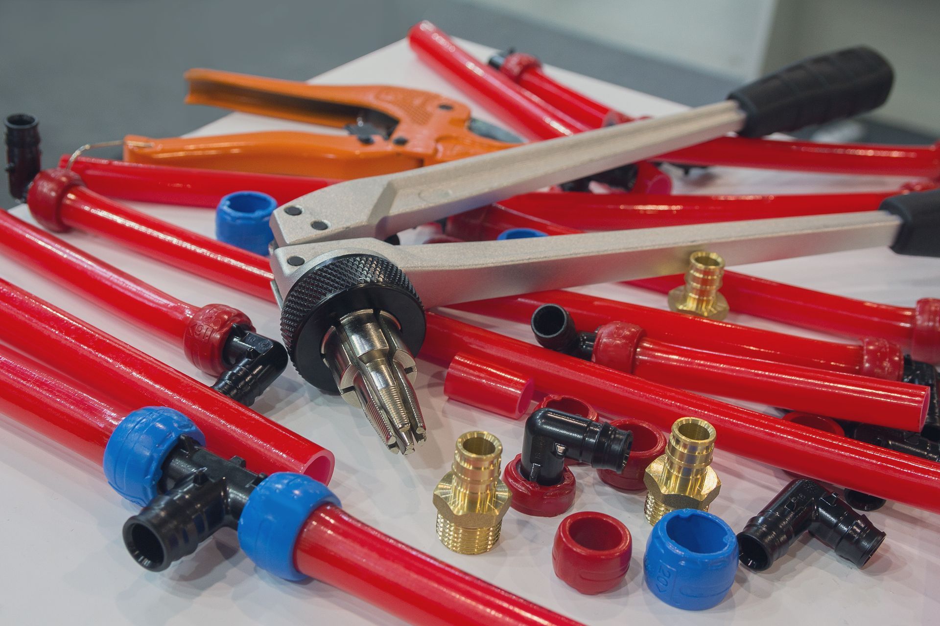 Colorful coils of PEX water pipes arranged on a table, accompanied by an assortment of mounting tools including clamps, brackets, and fasteners.