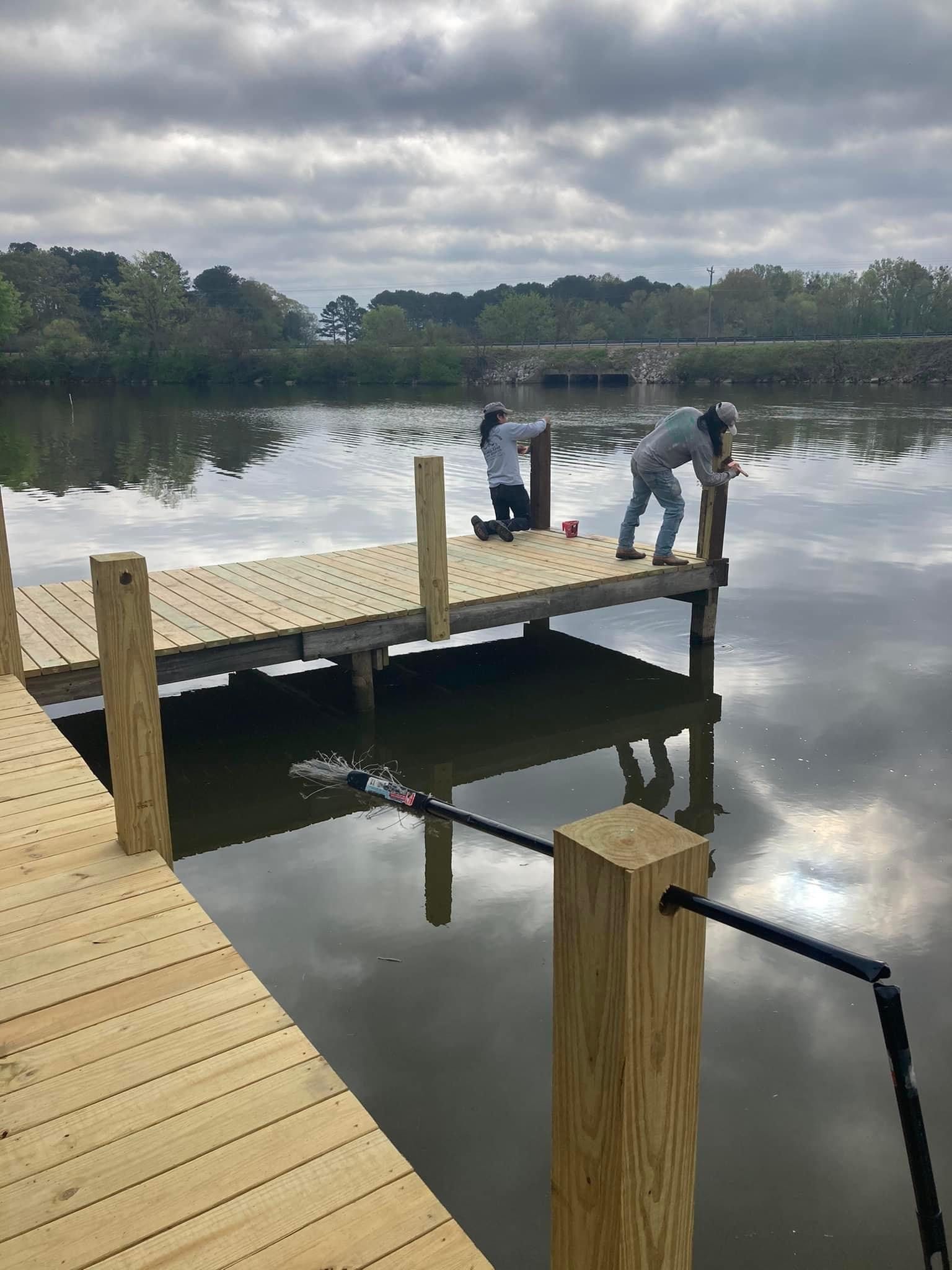 Two people are standing on a wooden dock overlooking a lake.