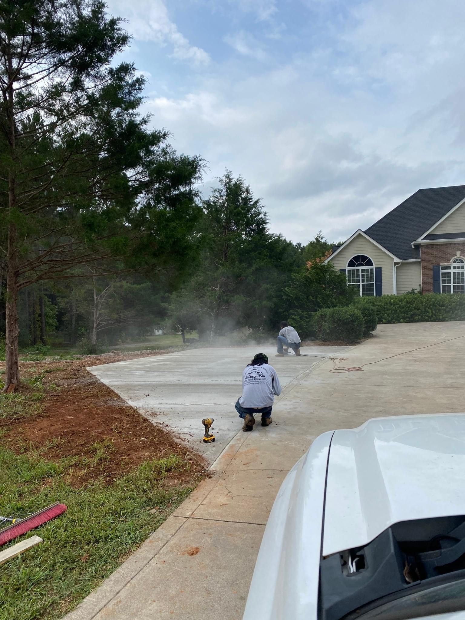 A man is kneeling on a concrete driveway next to a white truck.