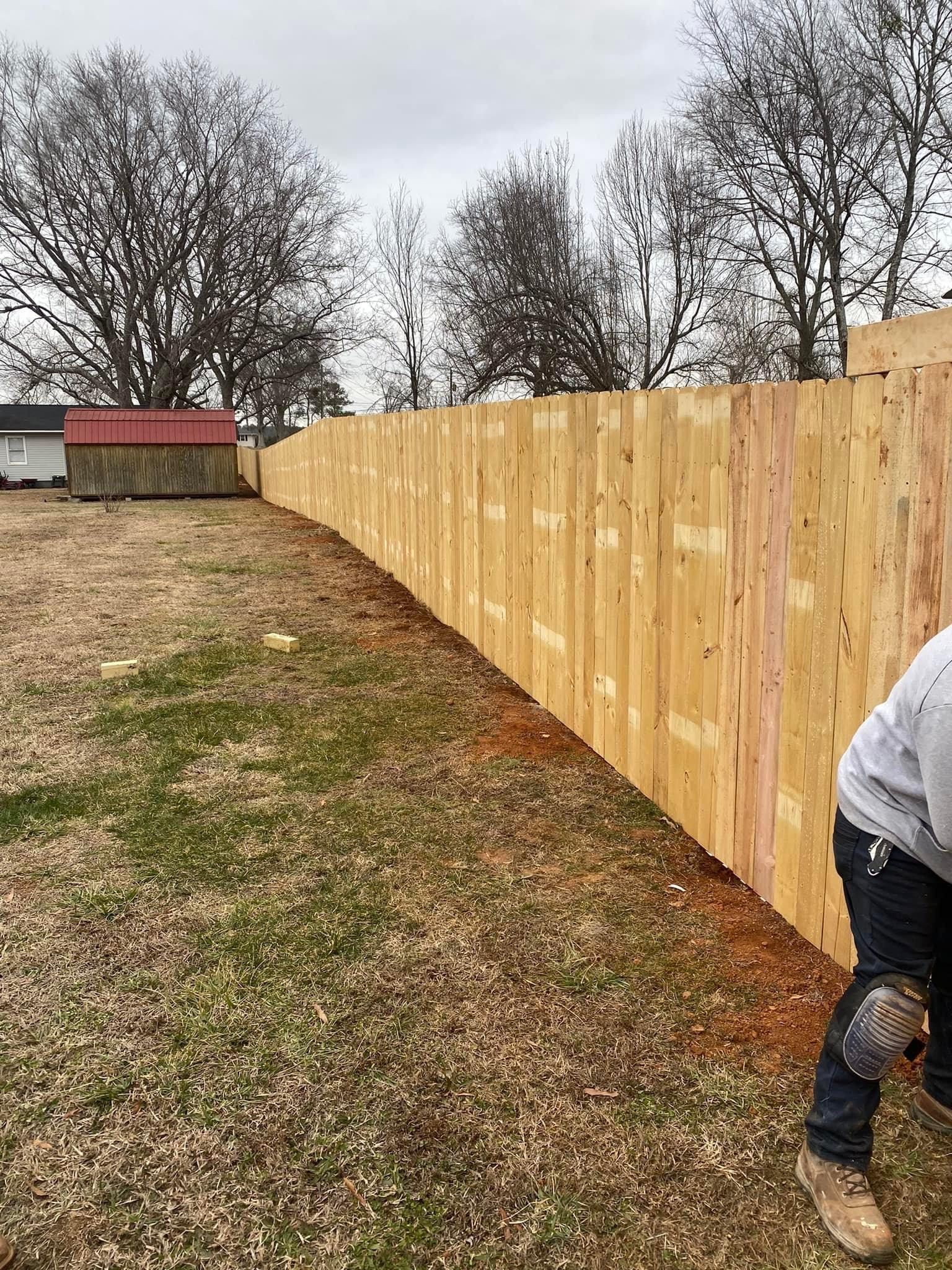 A man is standing next to a wooden fence in a yard.