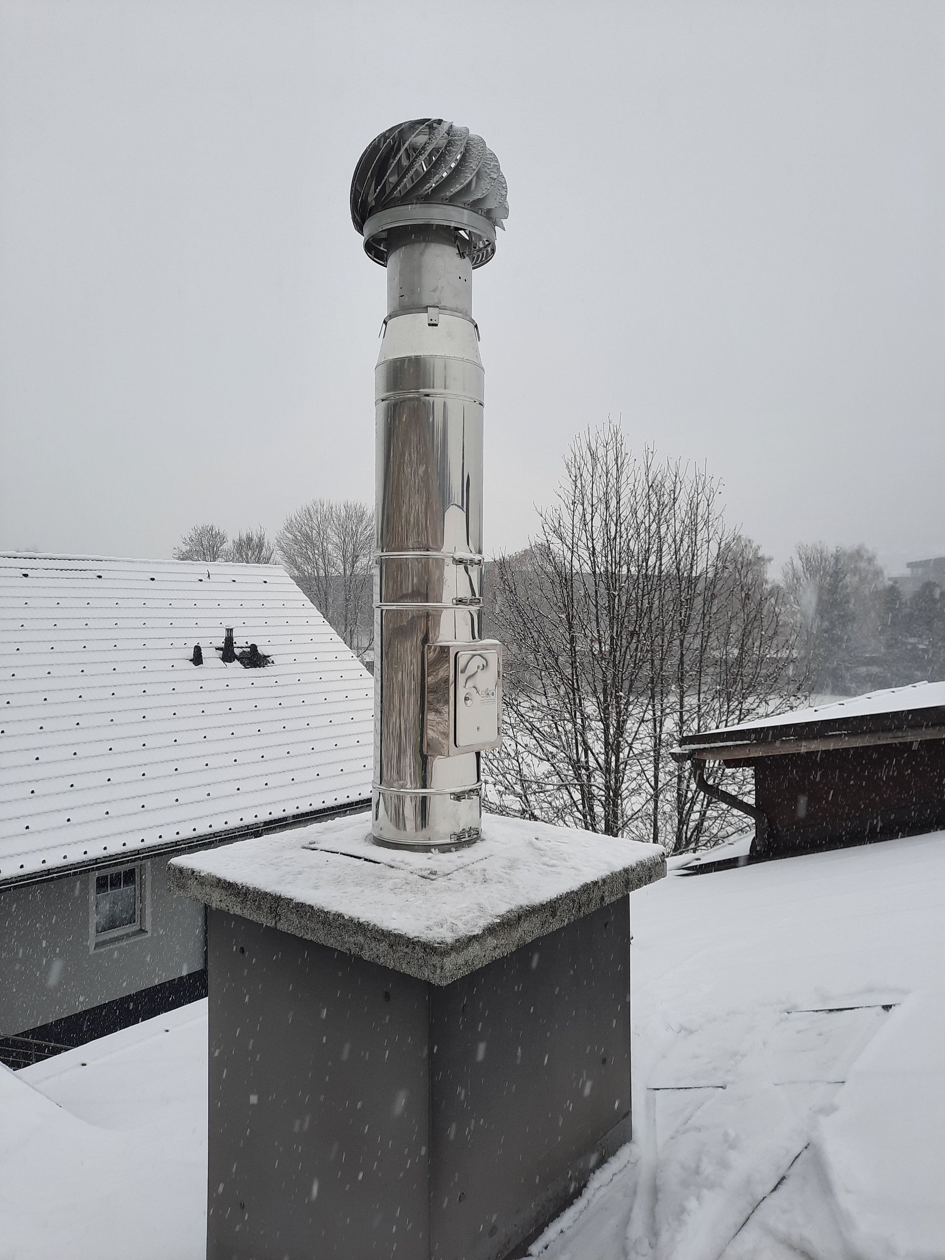 Auf einem schneebedeckten Dach sitzt ein Schornstein.