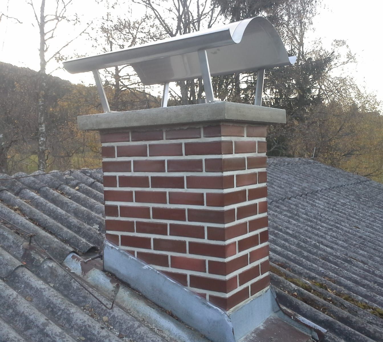 Ein gemauerter Schornstein auf einem Dach mit Bäumen im Hintergrund