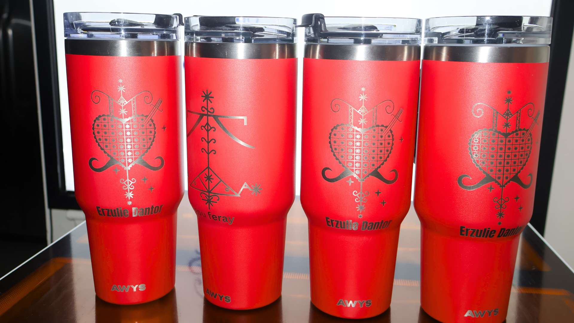 Four red insulated tumblers with silver etched designs and clear lids.