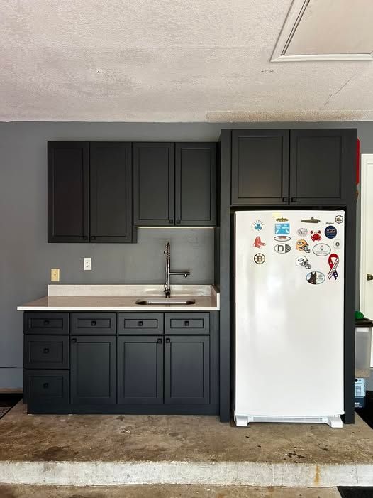 A kitchen with black cabinets , a sink , and a refrigerator.