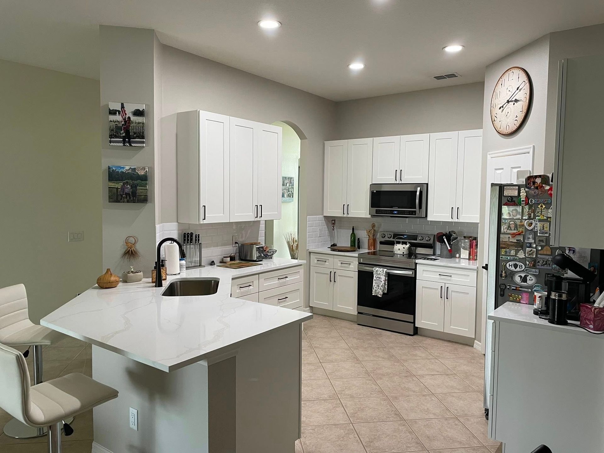 A kitchen with white cabinets and stainless steel appliances and a clock on the wall.